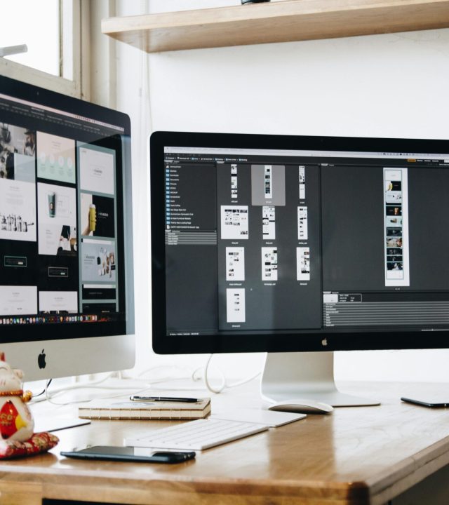 Stylish office workspace featuring dual monitors, a keyboard, notebooks, and decorative plant.